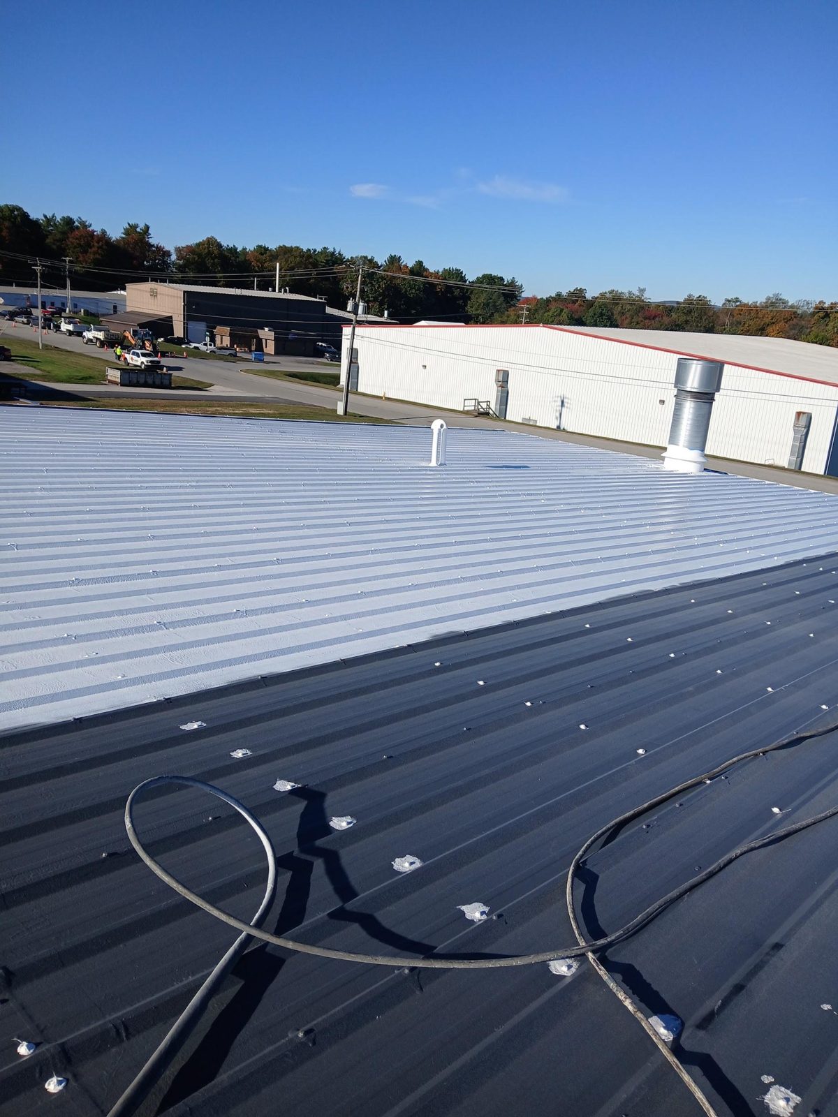 A commercial metal roof half coated in white, with the uncoated dark panels and sealed fasteners in the foreground