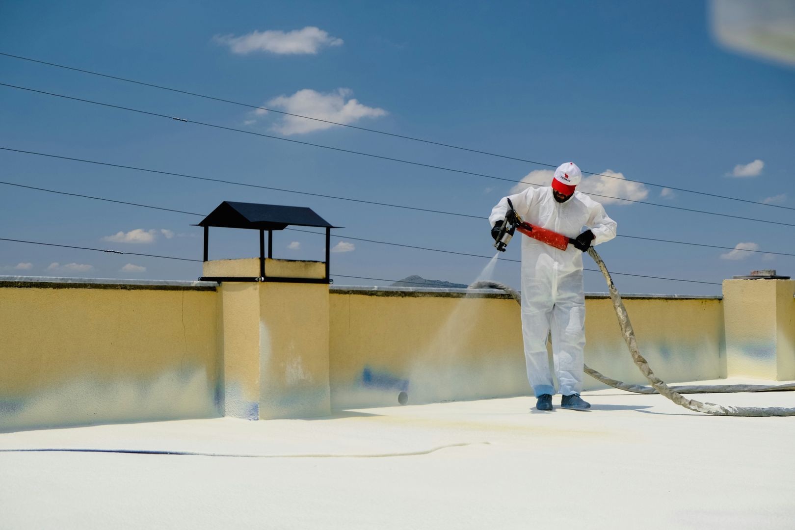 A roofer spray-applying a white coating system across a flat roof